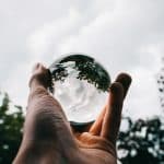 a person holding a glass ball with the reflection of beautiful green trees and breathtaking clouds
